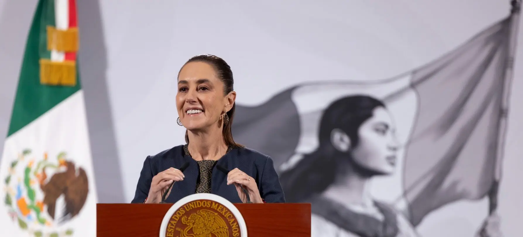 Woman speaking at podium with Mexican flag