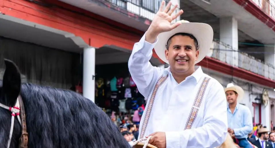 Smiling man in cowboy hat waving on horseback