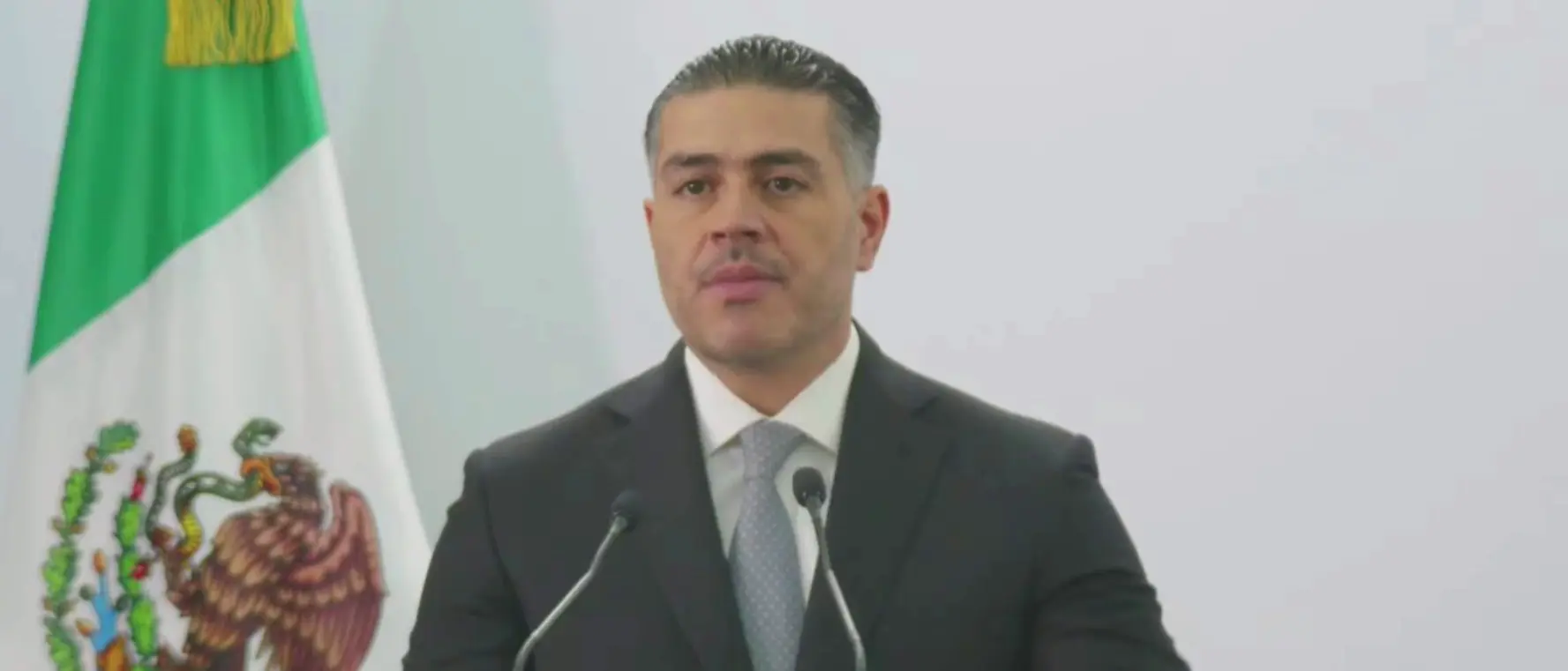 Speaker in suit at podium with Mexican flag