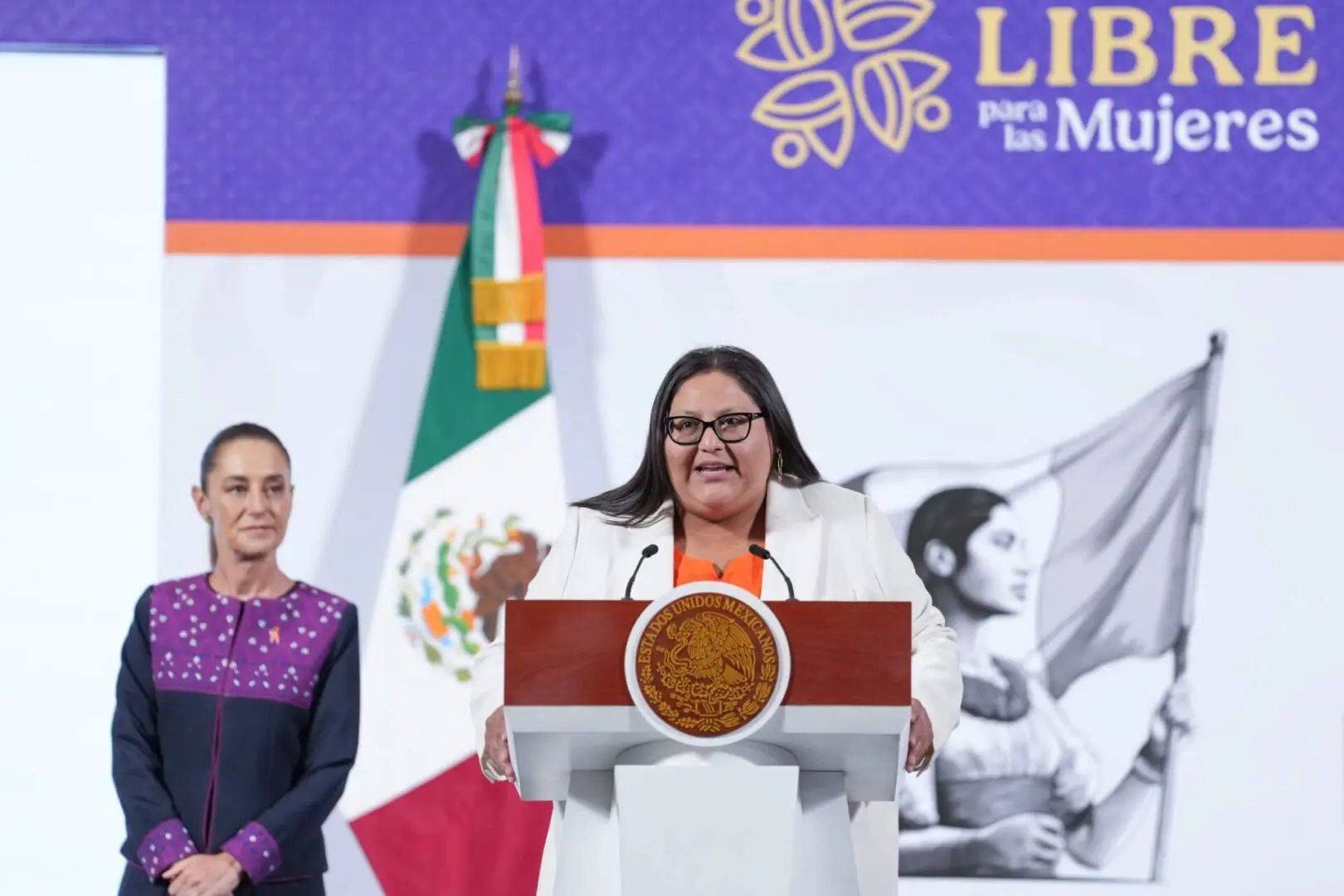 Woman speaking at podium with Mexican flag