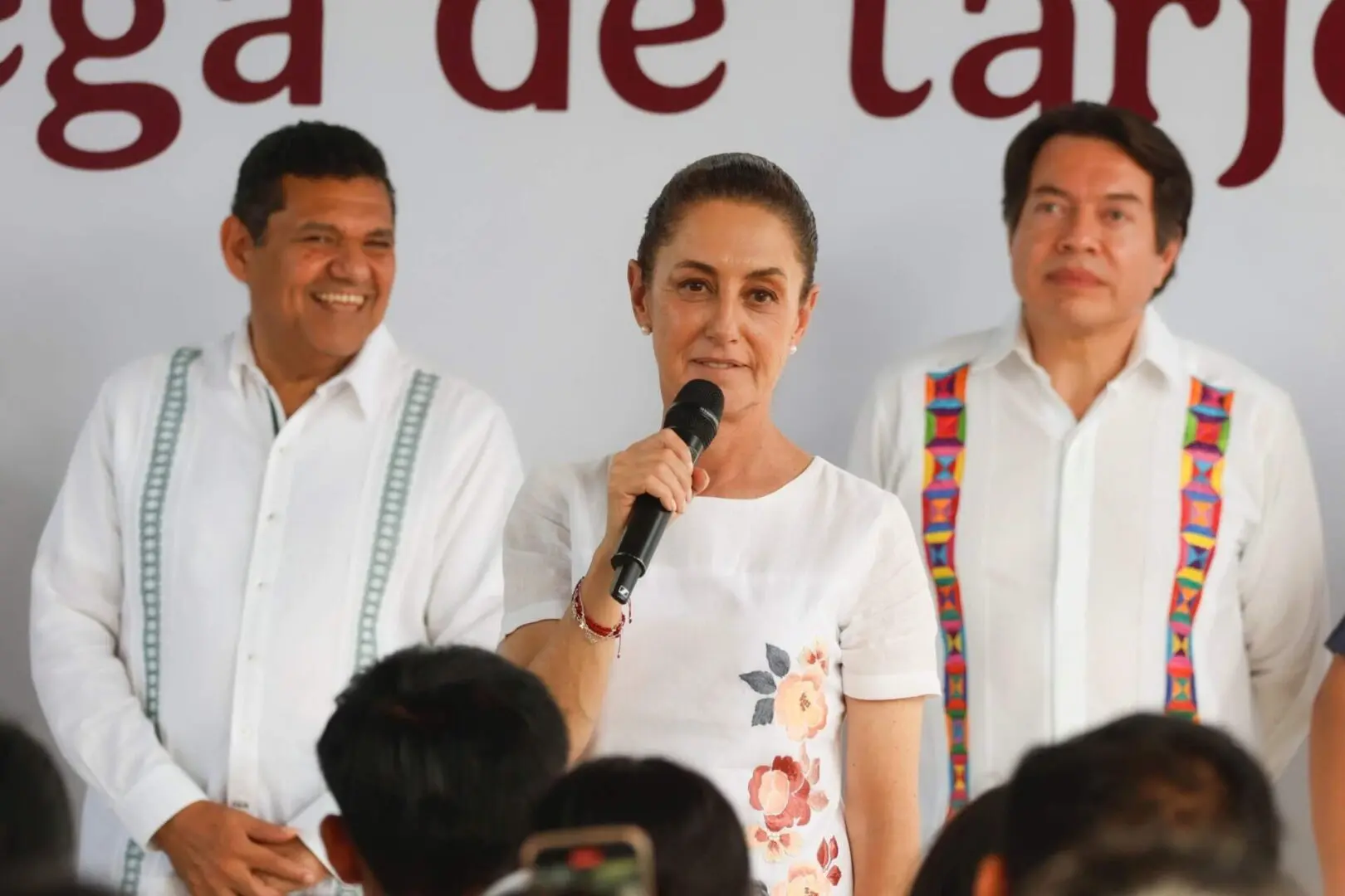 Woman speaking at event flanked by two men
