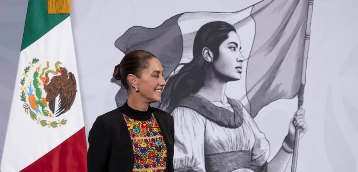 Woman smiling beside mural and Mexican flag
