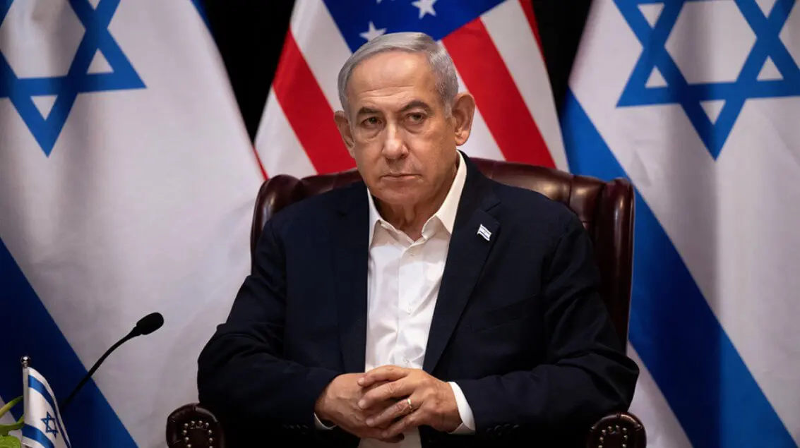 Male official seated before Israeli and U.S. flags