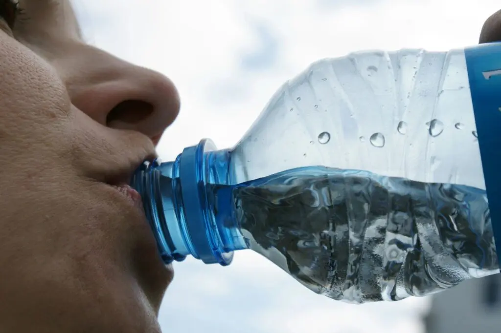 Persona bebe agua de botella de plástico, relacionada con la exposición a microplásticos
