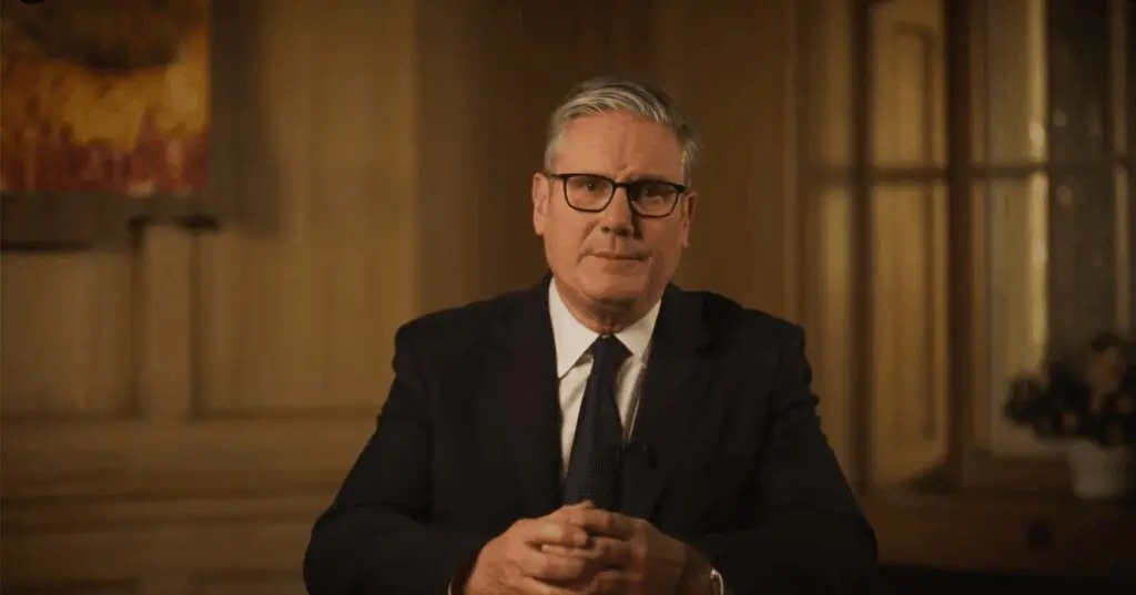 Man in suit and glasses seated, hands clasped