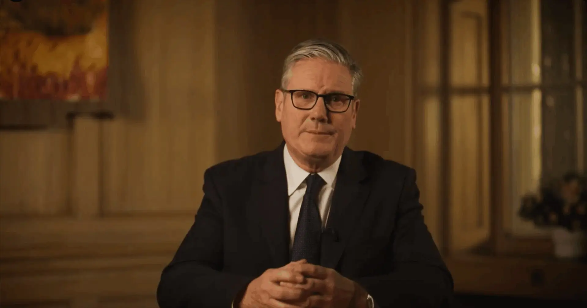 Man in suit and glasses seated, hands clasped