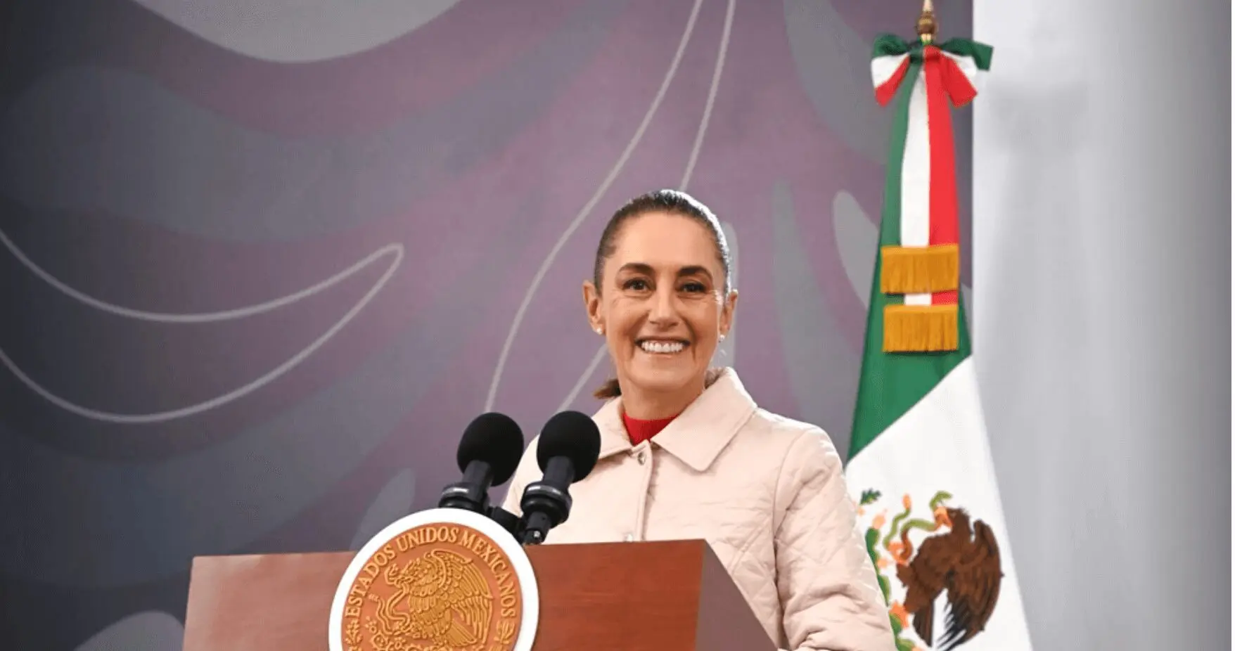 Smiling woman speaking at podium with Mexican flag