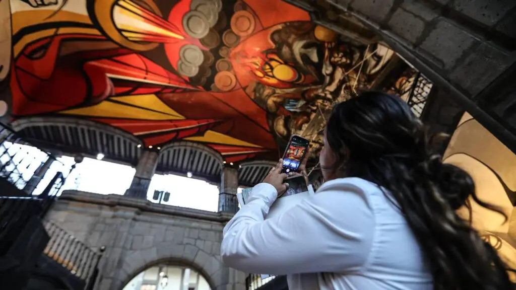 Mujer toma foto con celular de mural al interior de un museo.