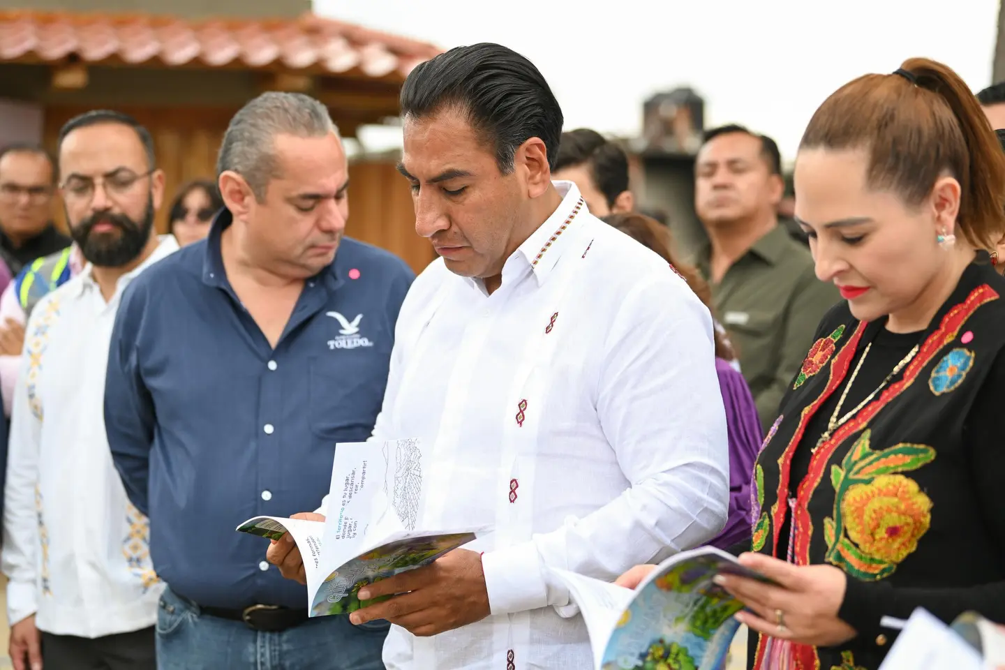 Gobernador de Chiapas consultado un folleto en sus manos, acompañado de personas.