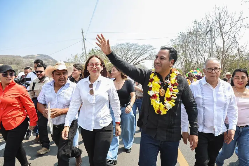 Gobernador de Chiapas extiende el brazo para saludar sobre carretera acompañado de funcionarios.