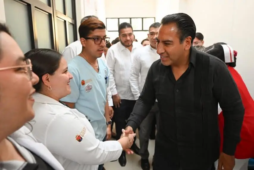 Político mexicano dándole la mano a una enfermera dentro de clínica.