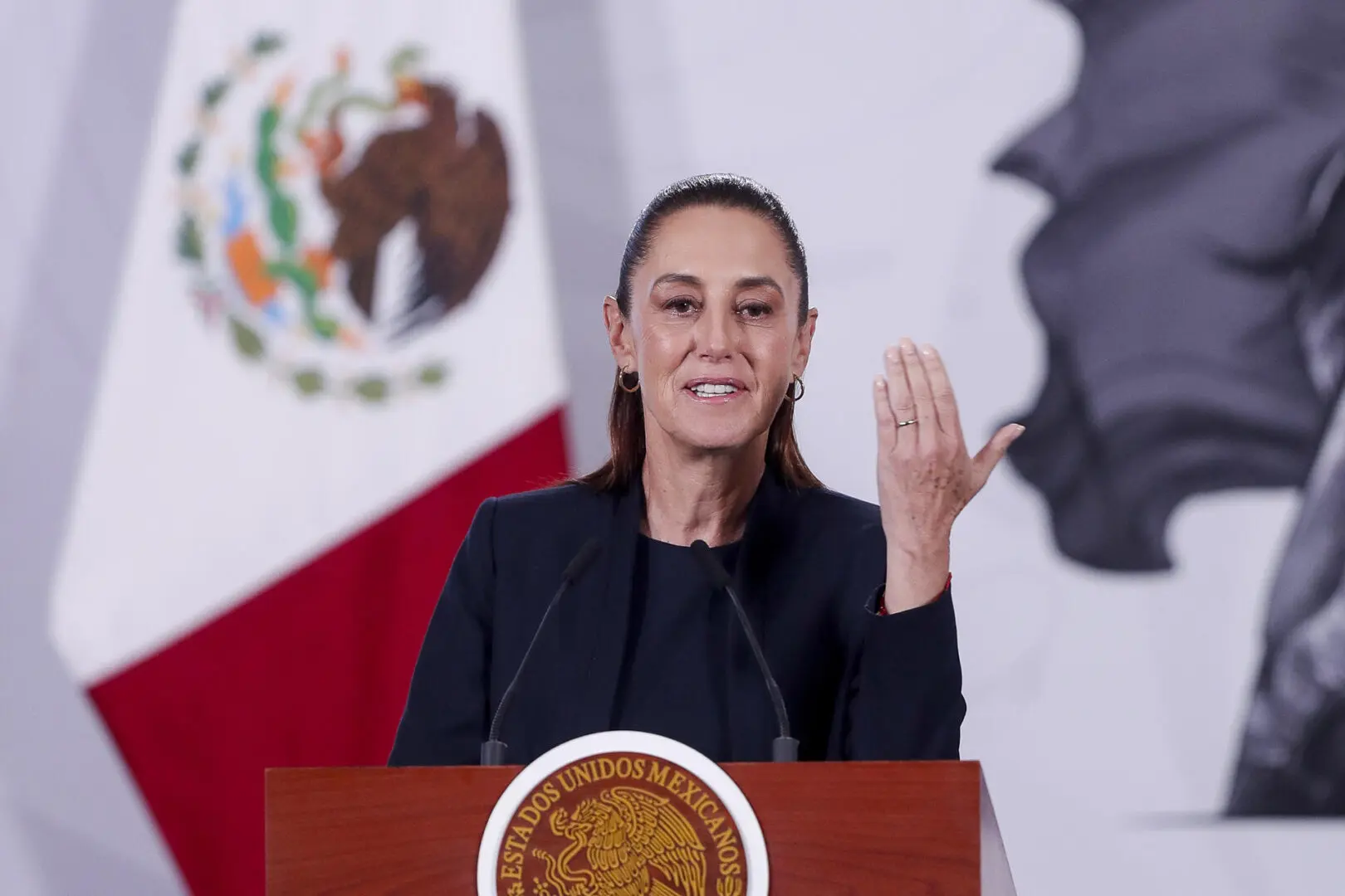 Presidenta de México alzando mano en conferencia.