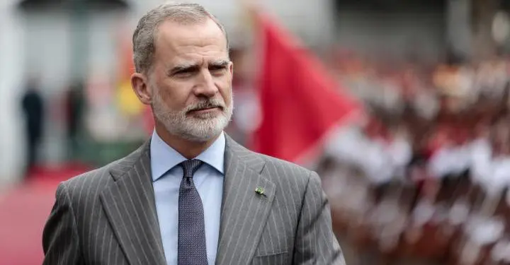 Rey de España frente a bandera roja con fondo borroso