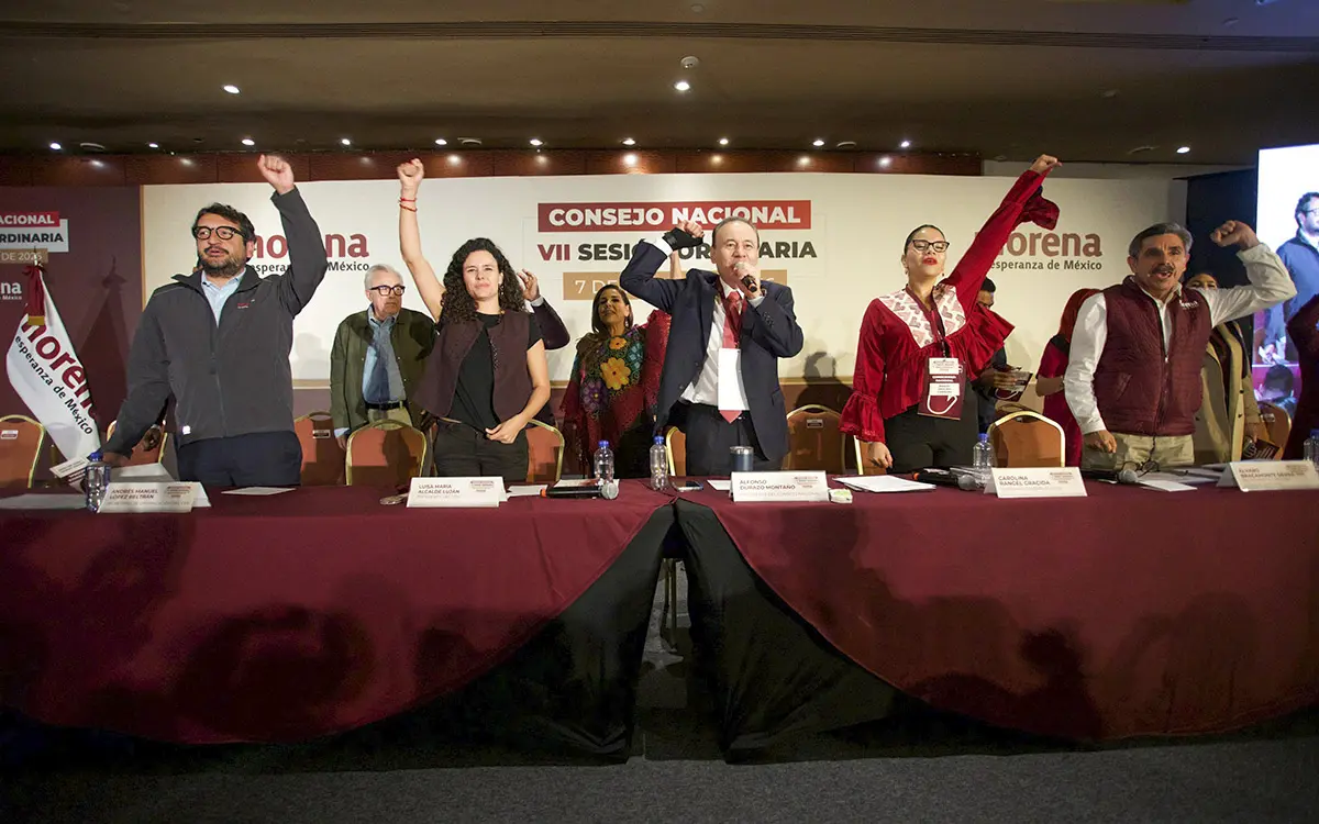 Políticos de Morena levantando brazo frente a mesa.