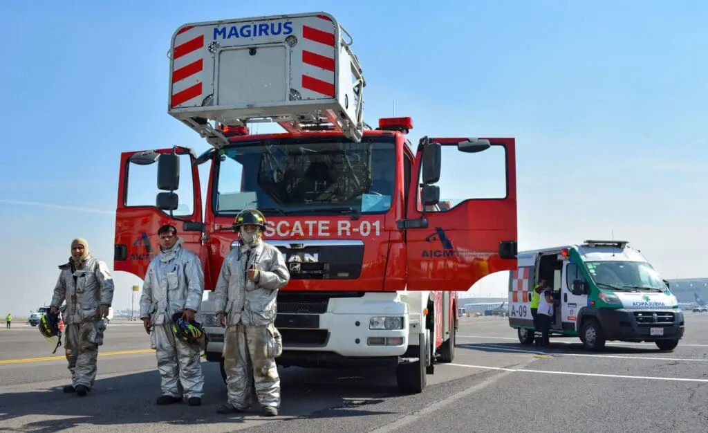 Firefighters in silver suits beside red firetruck