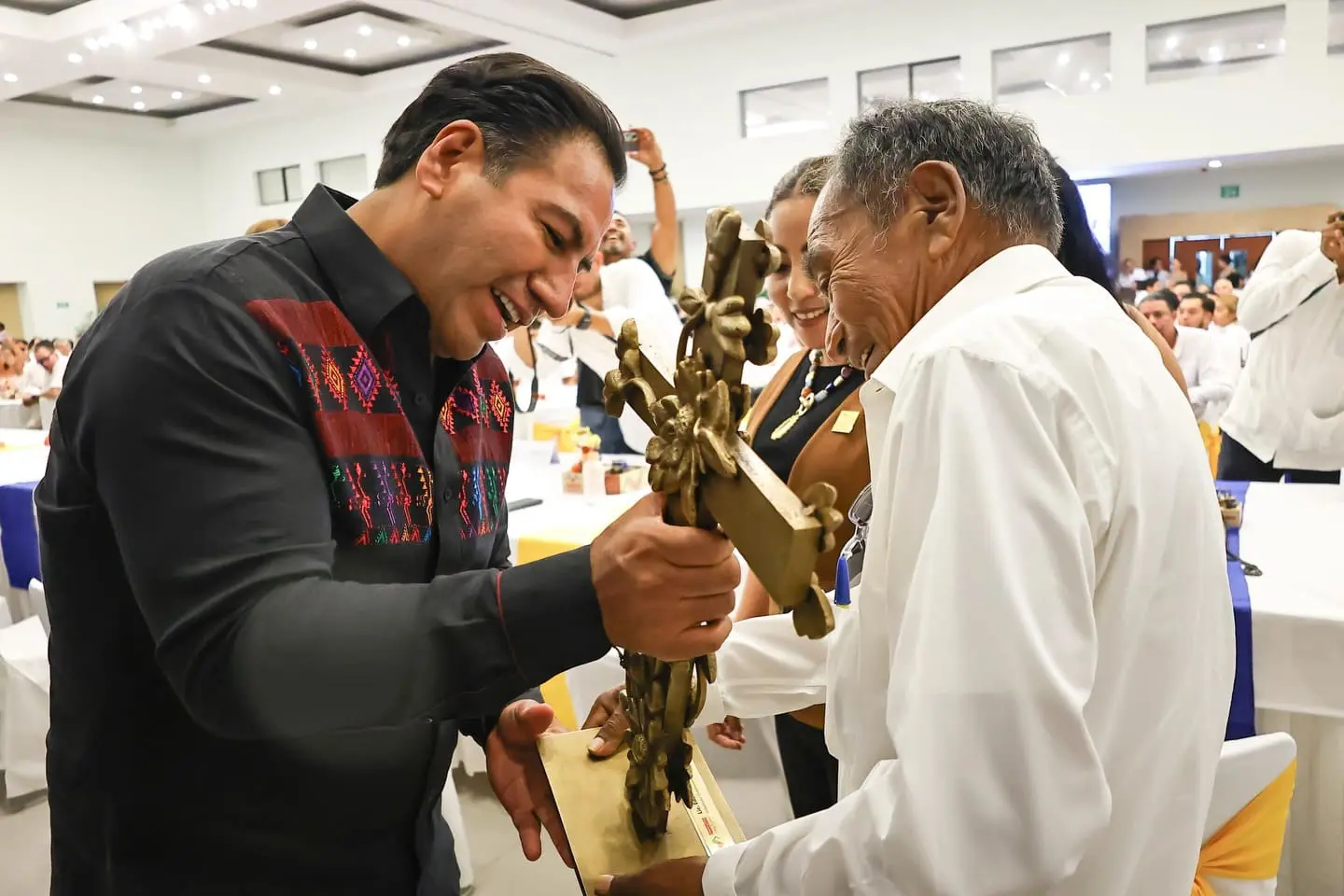 Two men smiling, holding golden sculpture