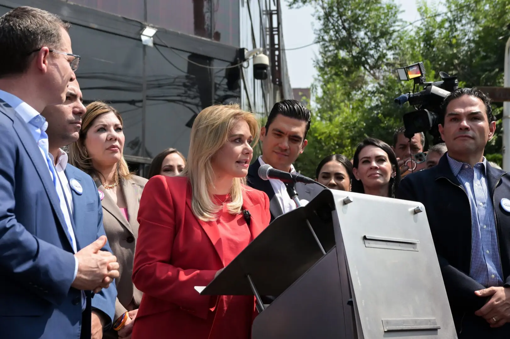 Woman speaking at podium surrounded by supporters