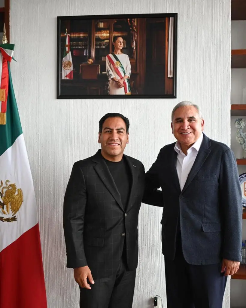 Two smiling men in suits beside Mexican flag
