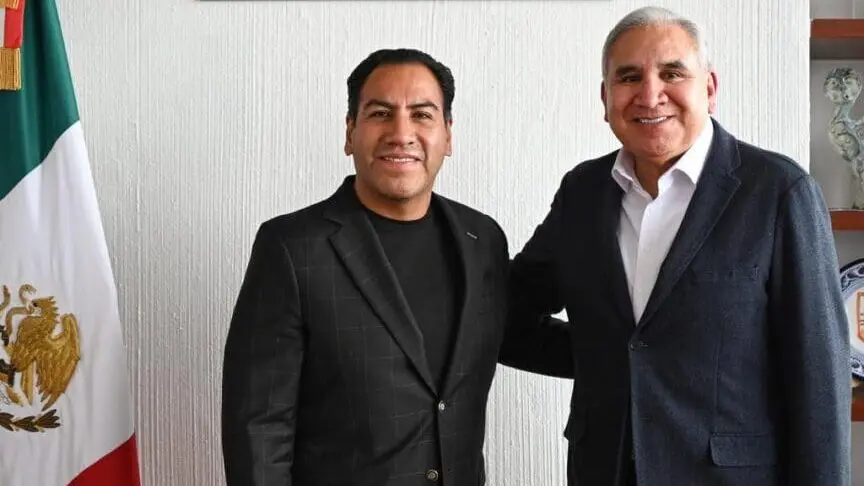 Two smiling men in suits beside Mexican flag