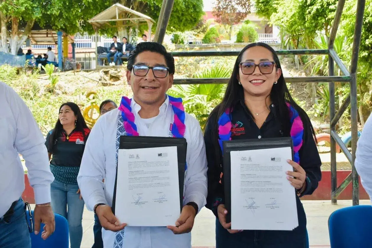 Two smiling people holding signed documents outdoors