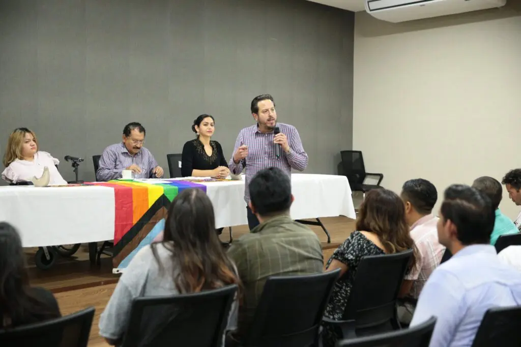 Speaker addressing audience at panel with pride flag