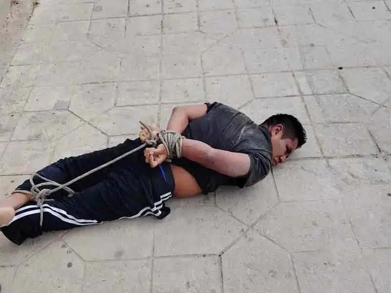 Person lying on pavement with hands tied