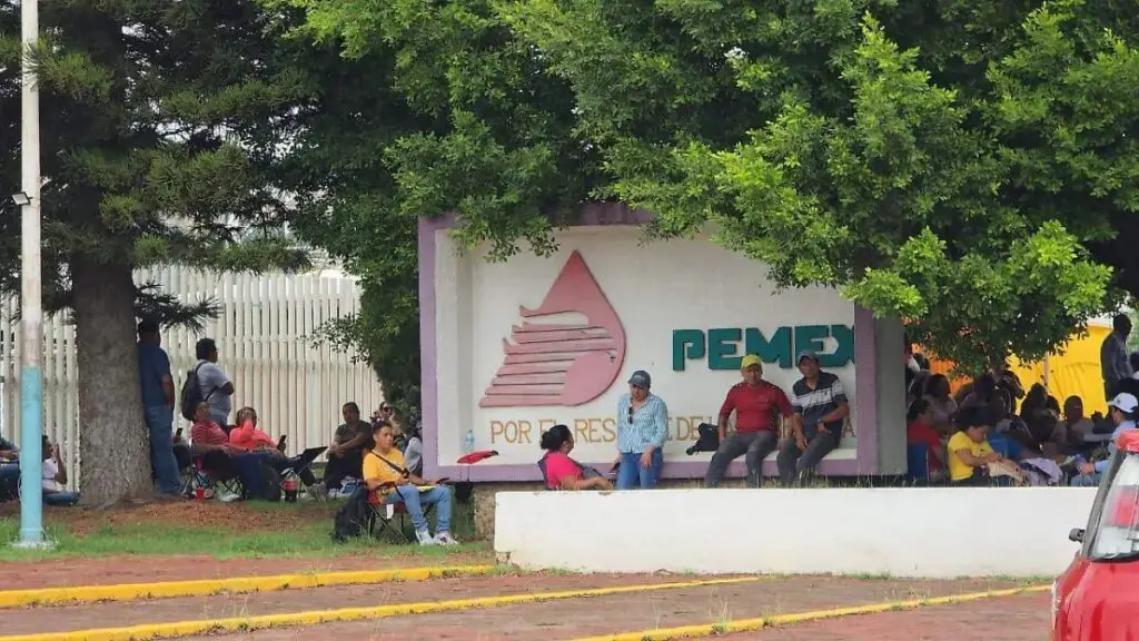 People seated under PEMEX sign and trees