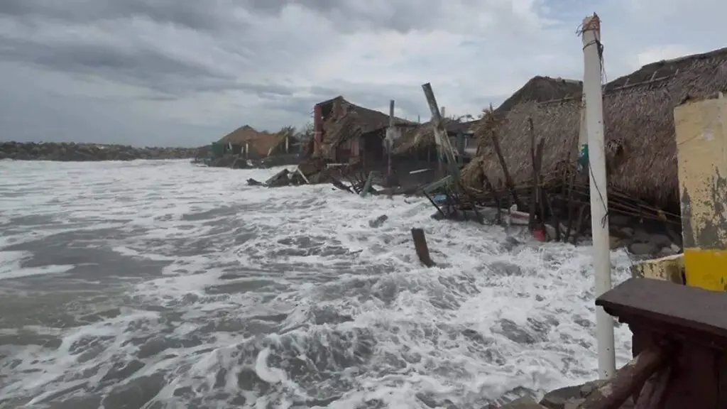 Waves eroding coastal huts under stormy gray sky