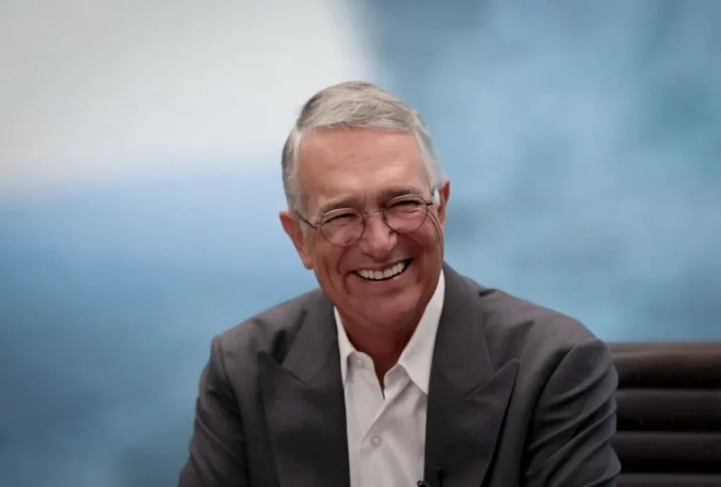 Smiling man in a suit, seated indoors.