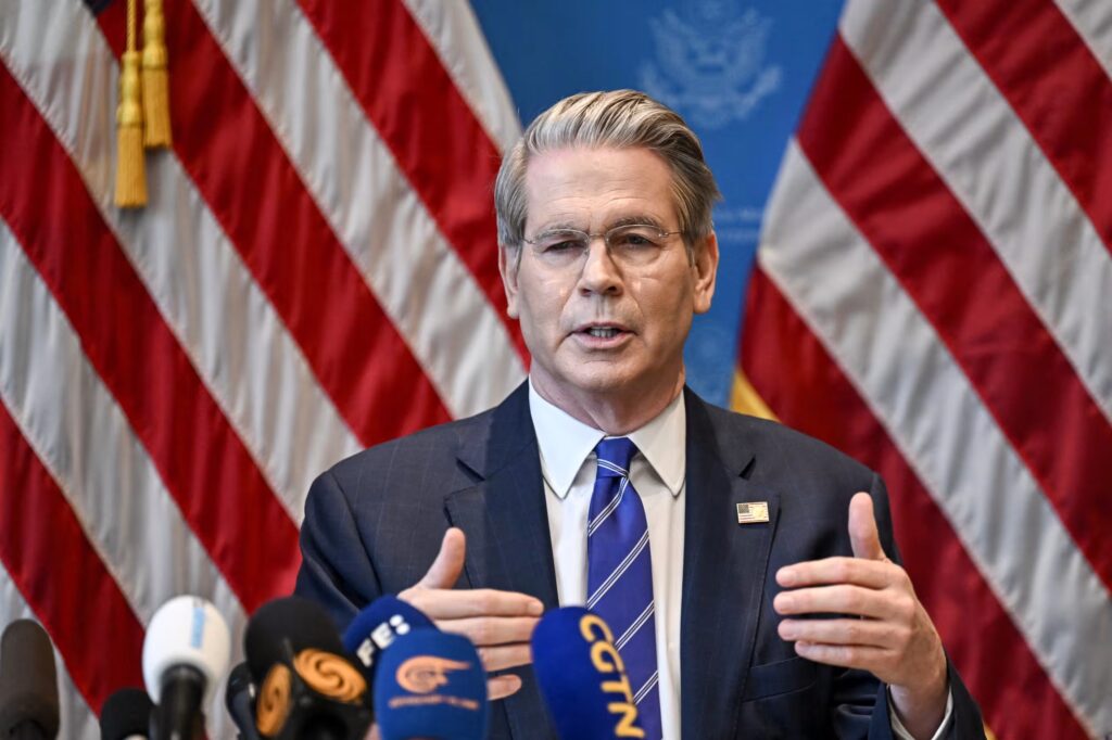 A man in a suit speaking in front of American flags.