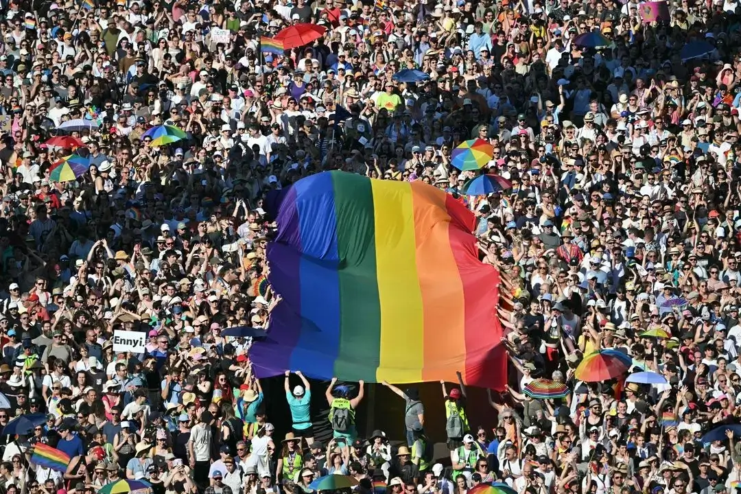 Large crowd with rainbow flag and umbrellas.