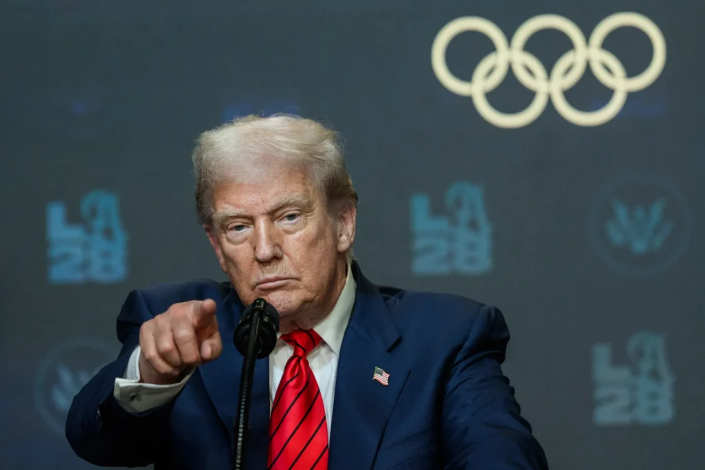 Donald Trump señala durante conferencia con el logotipo de LA28 y los aros olímpicos de fondo