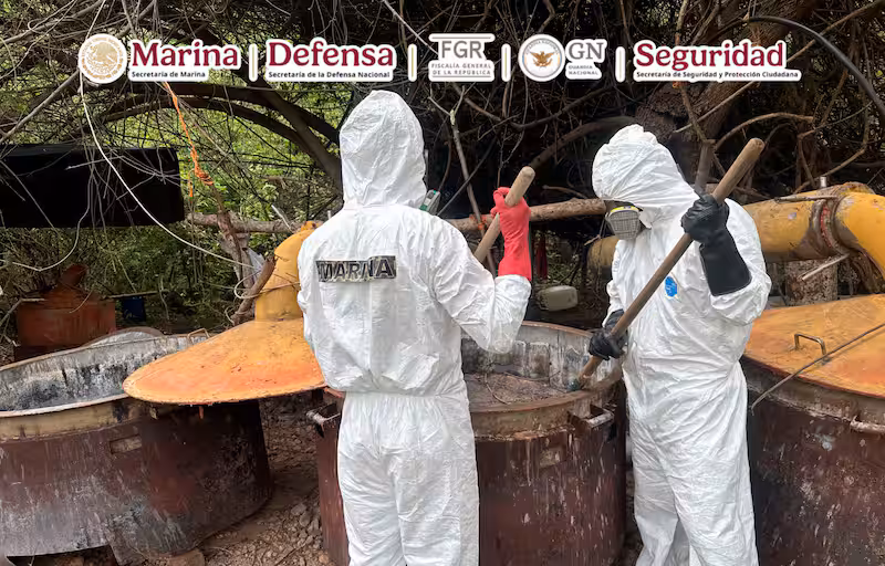 Dos personas con bata blanca investigan narcolaboratorio con contenedores al fondo