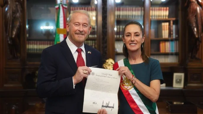 Funcionaria con banda presidencial posa junto a diplomático extranjero mostrando documento oficial en Palacio Nacional