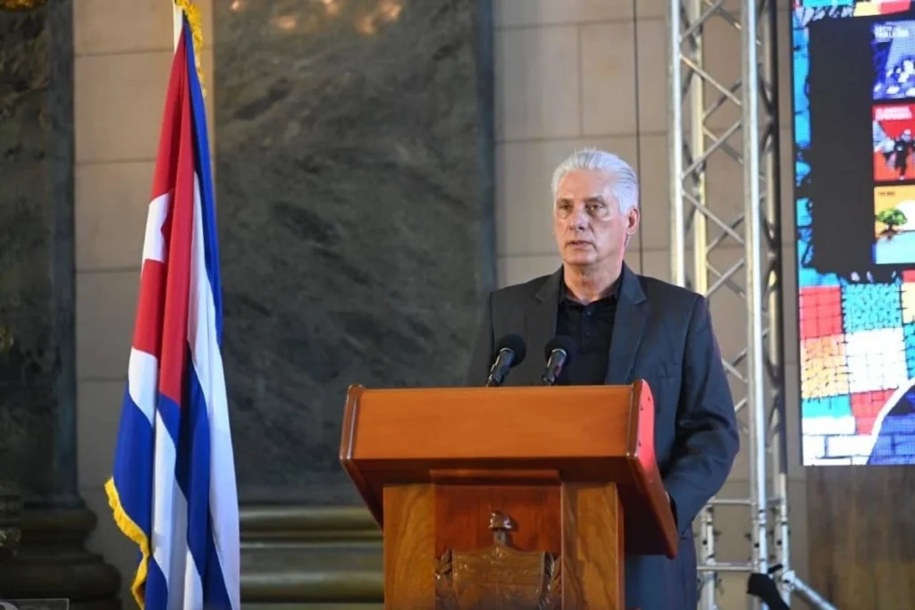 Man delivering speech at podium beside Cuban flag