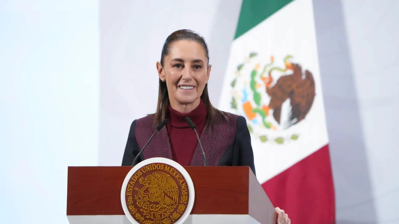 Claudia Sheinbaum frente a bandera mexicana y micrófono.