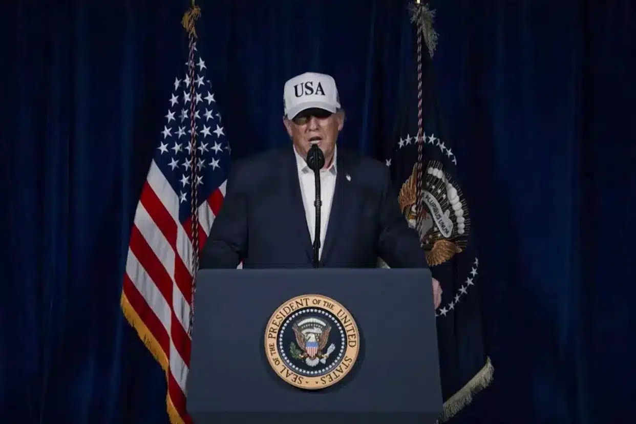 Presidente de EU frente a micrófonos y bandera.